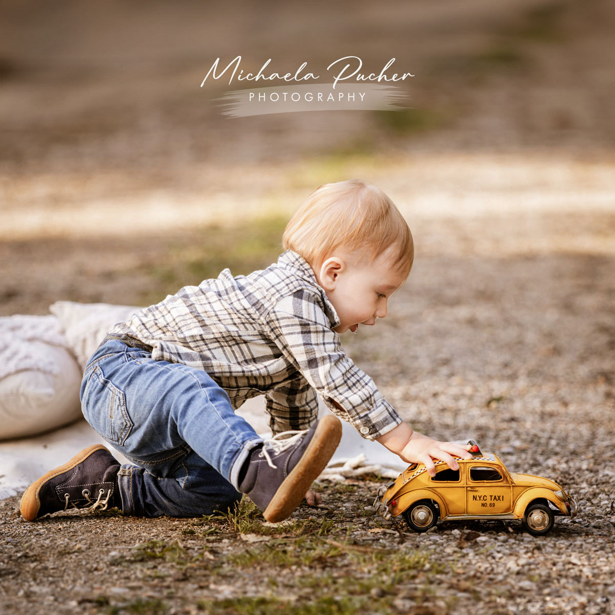 Kleiner Junge spielt draußen kniend auf dem Boden mit einem gelben Spielzeugauto im warmen Abendlicht.